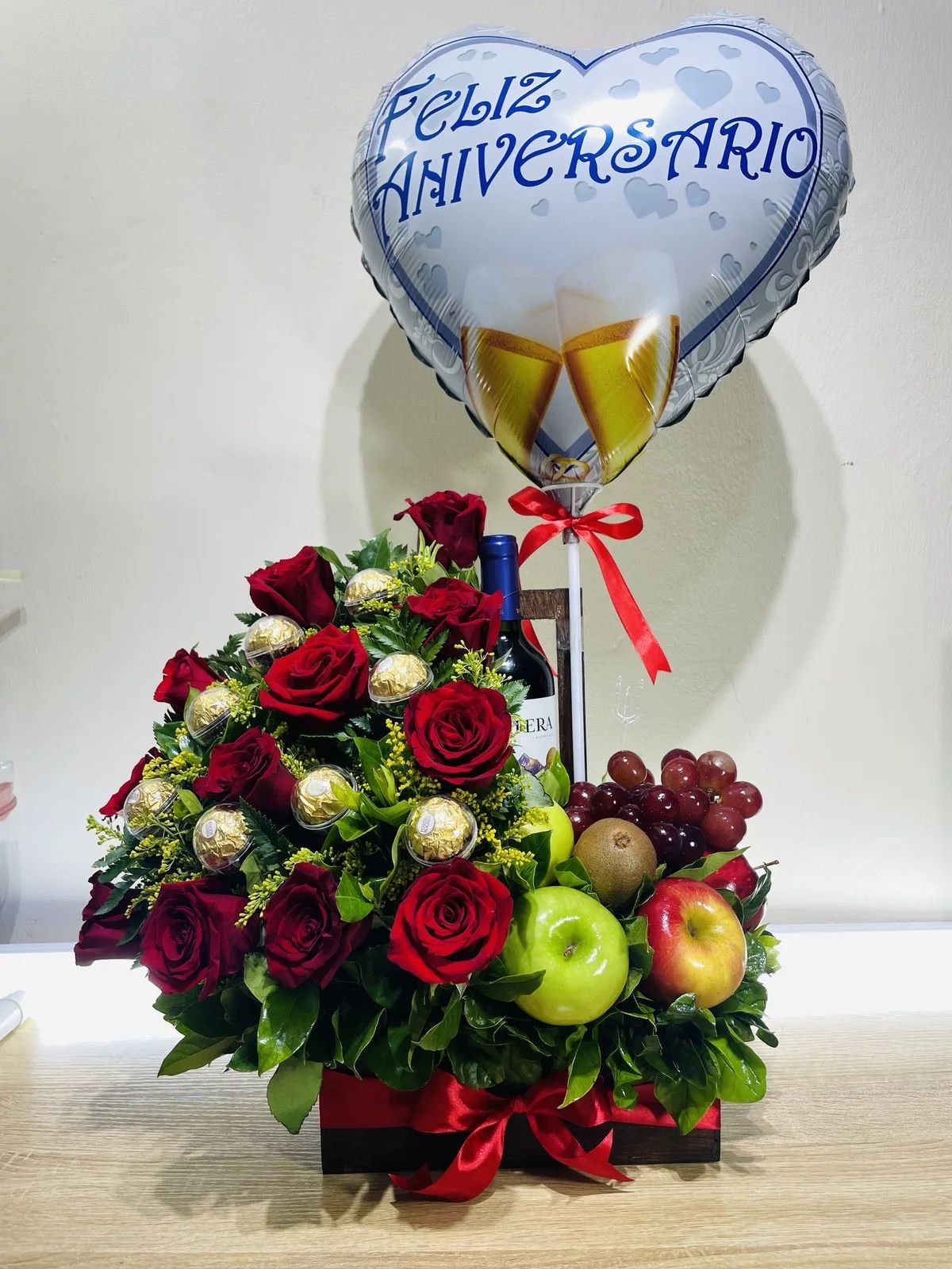Arreglo de aniversario con rosas, frutas, vino y un globo.