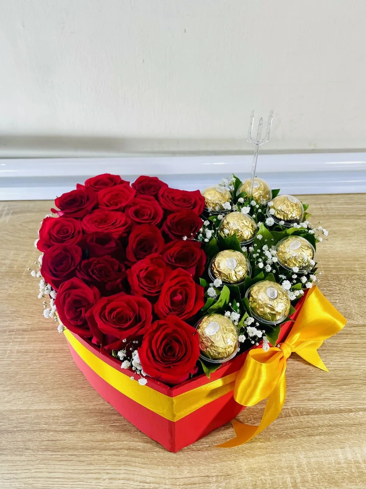 Corazón de rosas rojas con bombones dorados.